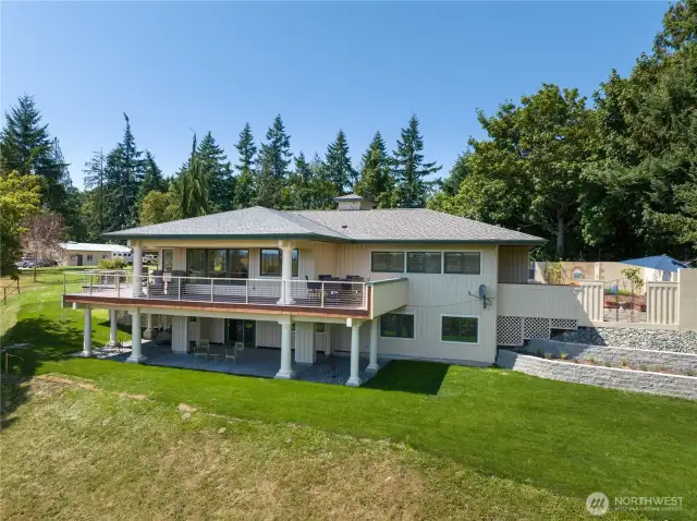 Here is the back side of the home with the secluded courtyards, fountains, and flowering gardens on the right side. The decking area continues around to the left side with the Koi ponds.  You can see the Barn in the background on the left side.  The organic garden is located between the main house and the barn.  There are fenced pastures in front.  Those chairs below are just outside the library.
