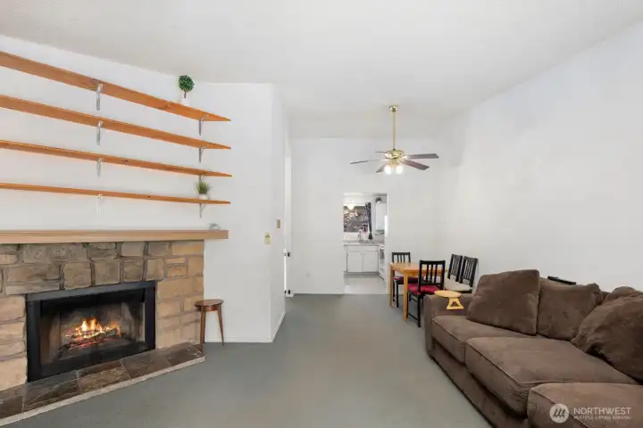 Open living and dining spaces centered around a stone fireplace and elevated ceilings.