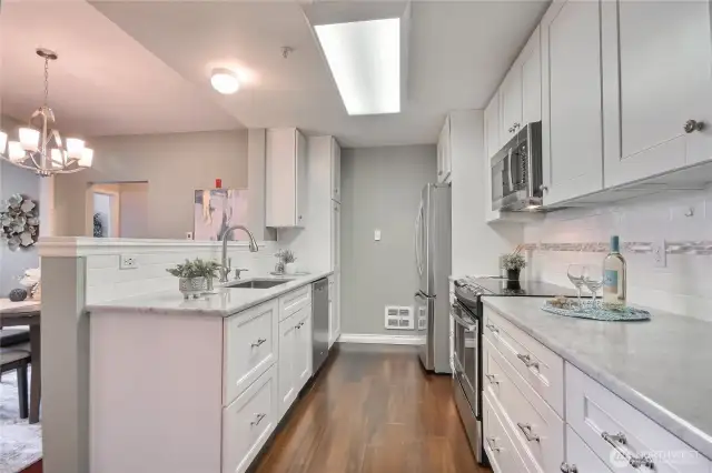 Remodeled kitchen features Carrera marble and quartz, undermount sink, white cabinets, and SS appliances.