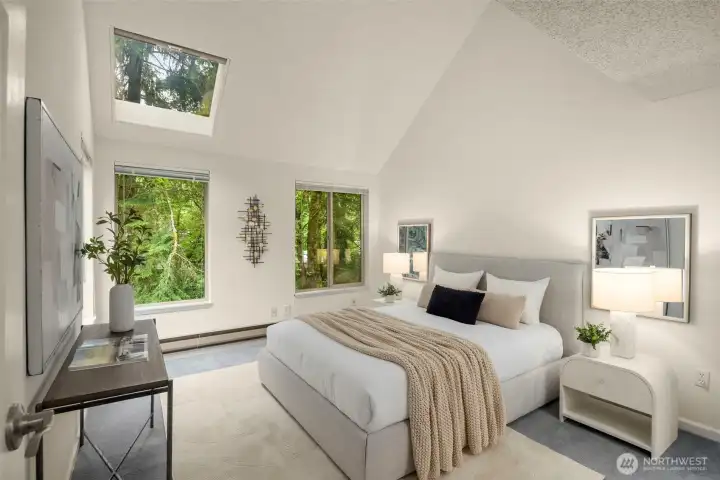 Airy primary retreat with soaring ceilings, skylight, and serene forest backdrop.