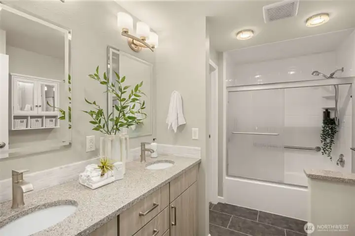 Beautifully updated bath with dual sinks, ample storage, and sleek shower — accessible from both the primary bedroom and hallway.