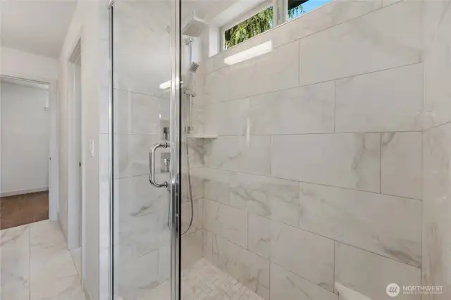Walk-in glass enclosed shower with tiled surround and rain shower and handle faucet.