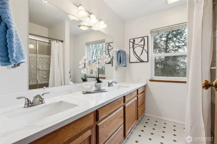 The primary bathroom features updated counters, dual sinks and a glass door, step-in jetted tub/shower combination plus views of the private portion of the lot beyond.