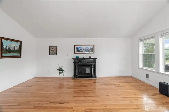 Open living area with gas fireplace & hardwood floors, lots of windows