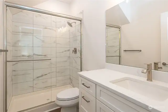 The Guest Bathroom boasts a sizable vanity with gorgeous quartz counters and a full tile shower with a sleek sliding glass door.