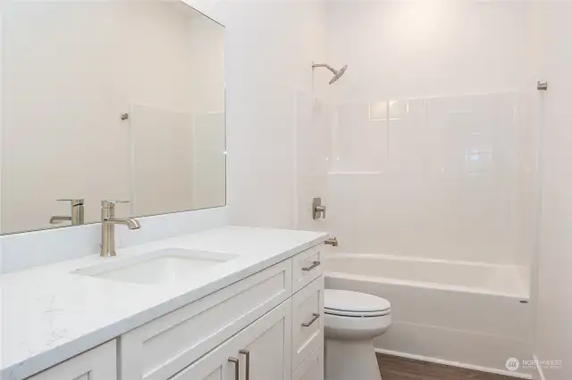 The Full Bathroom in the upstairs hallway boasts excellent storage space, quartz counters, a full bath/shower combo and luxury vinyl plank (LVP) flooring, blending modern style, durability and function.
