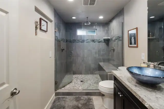 Updated bathroom features large luxurious tiled shower with three-showerhead setup and stylish vessel sink.