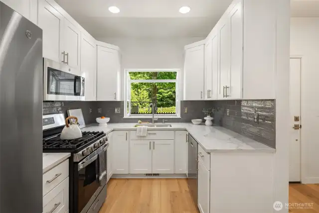 The gorgeous new kitchen boasts white shaker cabinets, a stylish tile backsplash, sleek white quartz countertops, modern fixtures, and stainless steel appliances—including gas cooking—for a perfect blend of elegance and function.