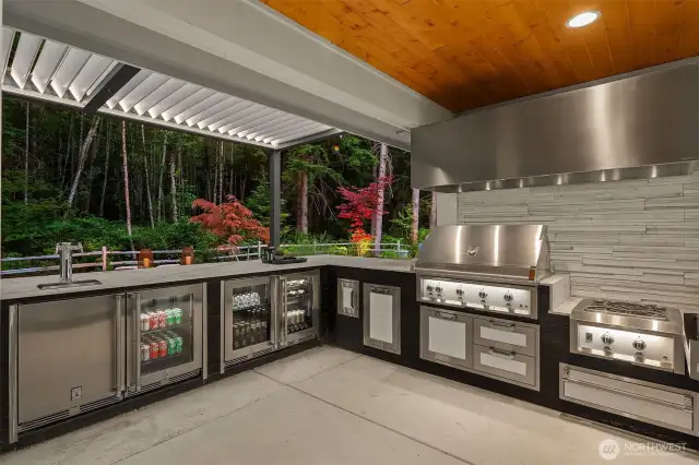 The outdoor kitchen is a true chef’s dream, equipped with top-of-the-line Hestan appliances. Enjoy a 42-inch grill, power burner, pizza oven, 24-inch double-tap beer dispenser, icemaker, and insulated sink. Two undercounter refrigerators with wine storage, a sealed pantry with double and single storage drawers, a trash/recycle center, and a powerful custom-vented hood complete this exceptional culinary space