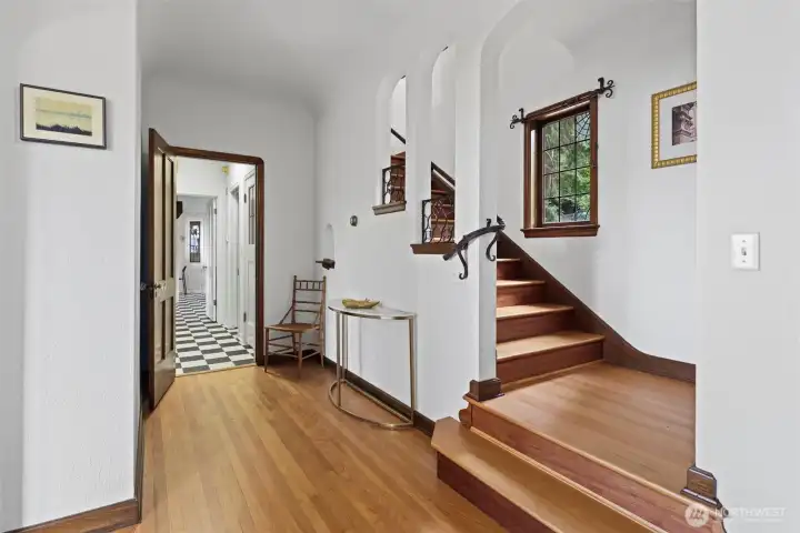 Entryway hallway and formal staircase feature the original railing, spiderweb stained glass window, and vintage curtain hardware