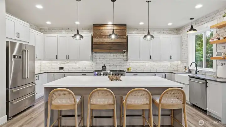 True entertainer’s kitchen with oversized island, custom hood, open shelving, quartz countertops, commercial appliances, walk-in pantry, and wine fridge.