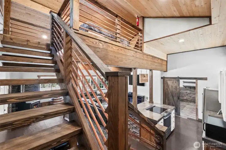 Staircase leading to loft with wood railing and open concept design.