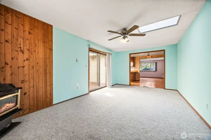 Cozy and flexible bonus room featuring a gas fireplace, ceiling fan, and skylight for year-round comfort and natural light. Direct access to the deck makes it perfect for entertaining or relaxing with family.