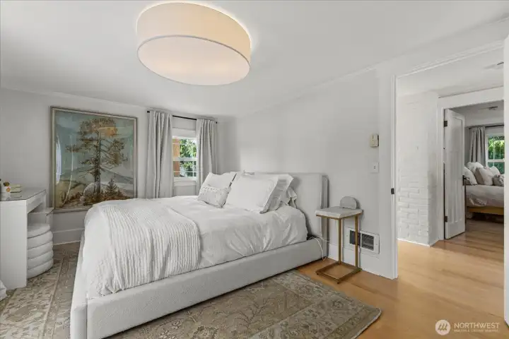 Another view of the primary bedroom and hallway, featuring beautiful millwork, hardwood floors, and white brick—full of character