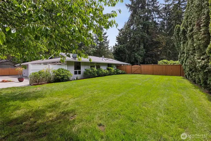 Side yard with grass, mature landscaping, and a fully fenced backyard for added privacy.