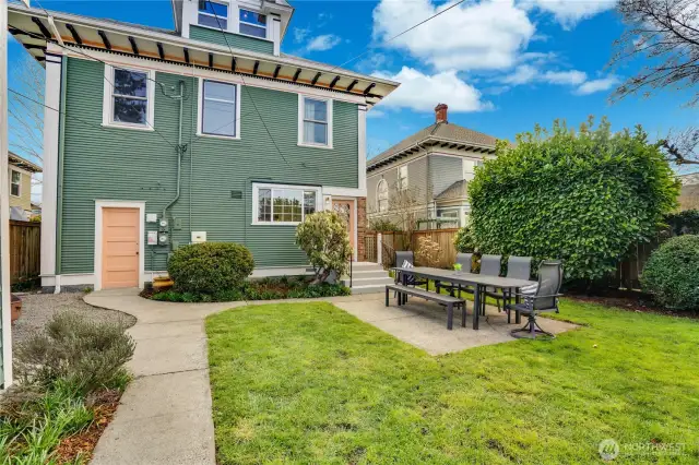 The fully-fenced back yard holds a detached garage, a patio, lawn, and paved pathways. A white dogwood, blooming cherry, laurel hedge, raspberries, and hydrangeas offer shade, color, and beauty in different seasons.