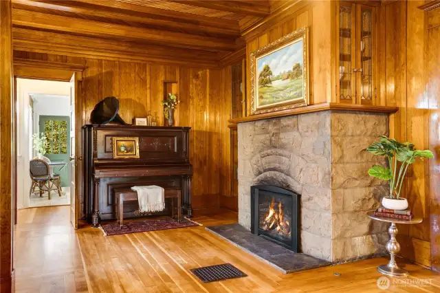 A second original stone fireplace draws the eye beyond the living room into the adjacent den. The homeowners installed a new gas fireplace for comfort. Notice the built-ins with leaded glass doors above the mantel.