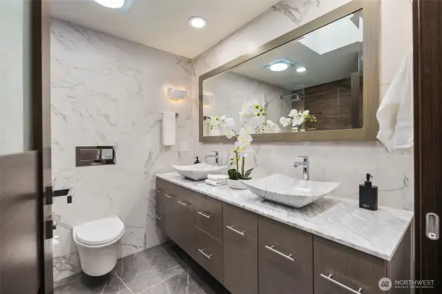 Natural light pours through the remote-controlled skylight, illuminating floating vanities, a dual rainfall shower, and radiant tile floors that keep every step warm and comfortable.