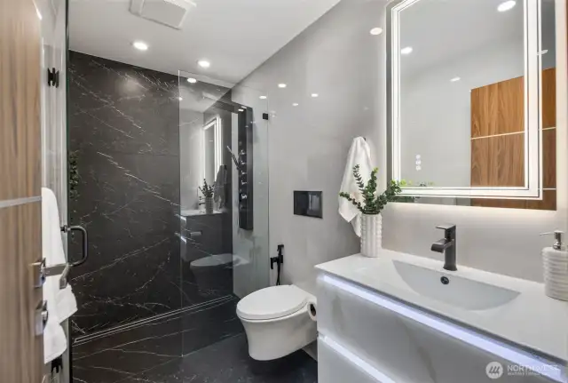 Black stone, crisp designer tile, and built-in LED lighting create a balance that feels both luxurious and innovative.