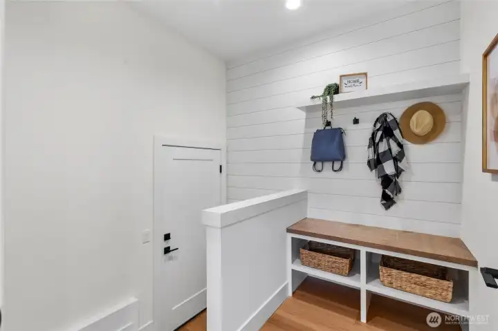 This charming mudroom blends practicality with style, offering a clean and organized space for everyday essentials. With woven baskets tucked into open cubbies, a sleek wooden countertop, and a wall-mounted shelf for decor and hanging items, it’s the perfect drop zone for busy days. The white shiplap walls and warm wood flooring add a cozy, welcoming touch to this hardworking corner of the home.