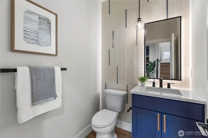This guest bathroom combines sleek design with thoughtful details, creating a space that’s both stylish and welcoming. The blue vanity adds a pop of color against the neutral tile backdrop, while the backlit mirror and pendant light offer a soft, modern glow. Clean lines, layered textures, and curated accents make it a standout feature for visitors.