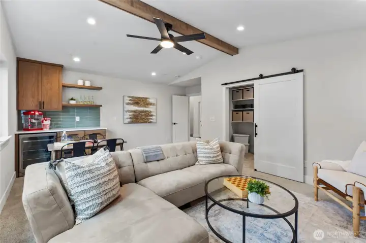 This entertainment room combines relaxed comfort with modern style, featuring a spacious layout, cozy seating, and a ceiling fan mounted on a warm wood beam for added character. With a built-in bar, dining area, and inviting atmosphere, it’s perfectly designed for hosting, lounging, or game night gatherings.