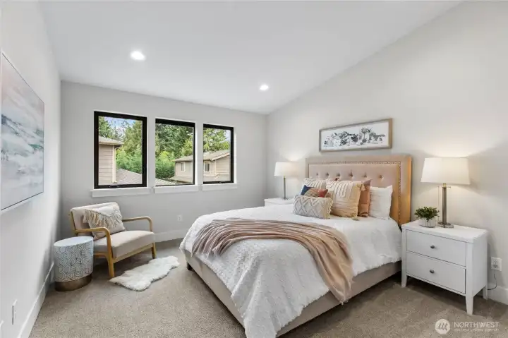 This bedroom exudes warmth and elegance with its soft blush accents, and cozy reading nook. Natural light pours in through large windows, enhancing the serene palette and inviting atmosphere.