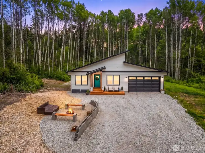 The long gravel drive winds through a canopy of seasonal color, arriving at a thoughtfully designed home surrounded by towering trees and peaceful forested scenery.