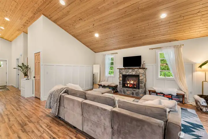 Anchored by a striking river rock fireplace, this inviting living space combines warmth, scale, and simplicity beneath expansive vaulted wood ceilings.