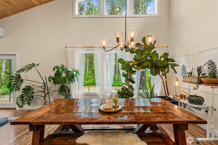 Vaulted ceilings and expansive windows fill this inviting dining space with natural light and a seamless connection to the surrounding forest