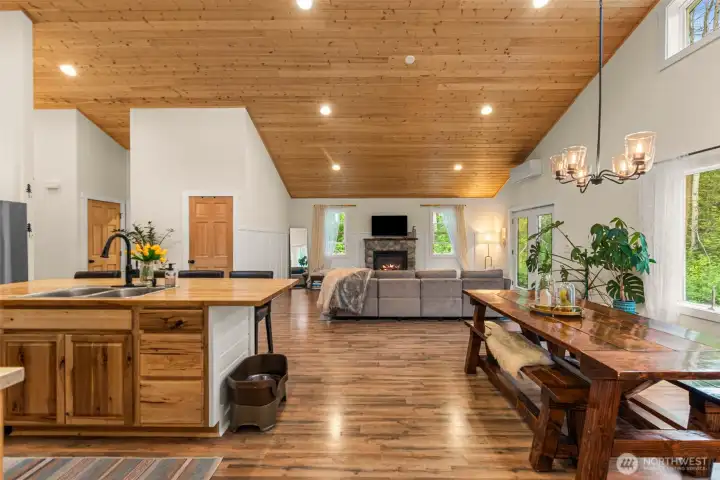 esigned with an emphasis on openness and gathering, this expansive great room seamlessly connects the kitchen, dining, and living spaces beneath soaring wood-clad ceilings that bring warmth and architectural character throughout