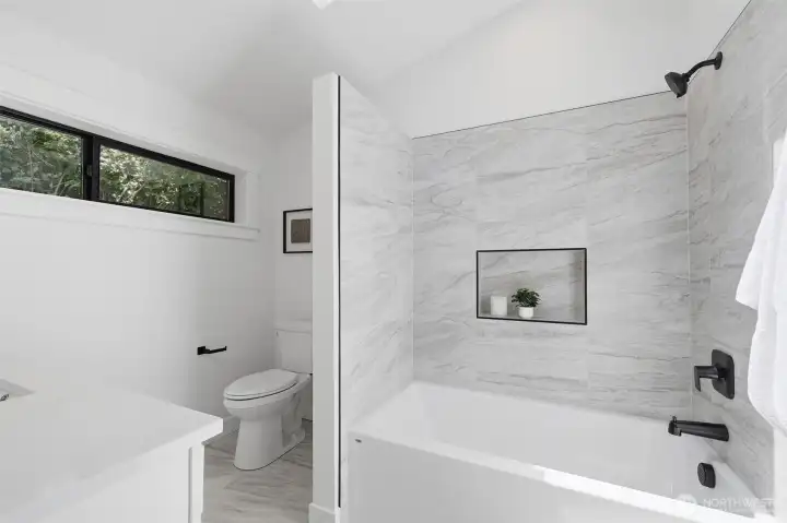Spacious second-floor bathroom featuring a large soaking tub, nook, vaulted ceilings, and a skylight that provides abundant natural light.