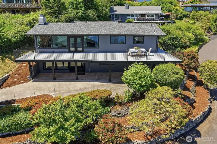 Showcases the rear exterior, featuring an expansive deck, a covered patio perfect for year-round entertaining, and stunning water and mountain views.