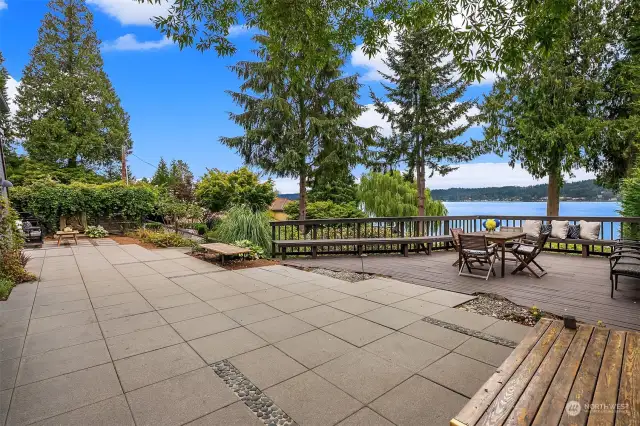 Massive paver patio with adjoining deck cantilevered over the lush garden.