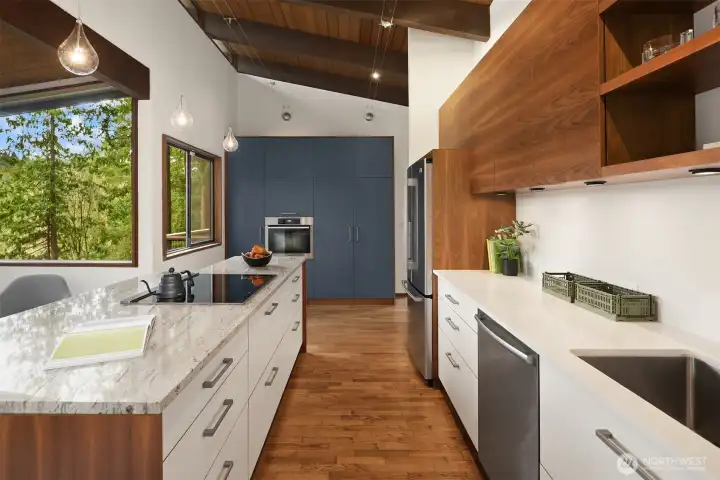 A custom Henrybuilt kitchen looks like it belongs in a home twice this price, with a bounty of clever and beautiful storage.  A wall of dusky blue houses the oven and pantry, and delivers a colorful pop against the walnut and white cabinetry.