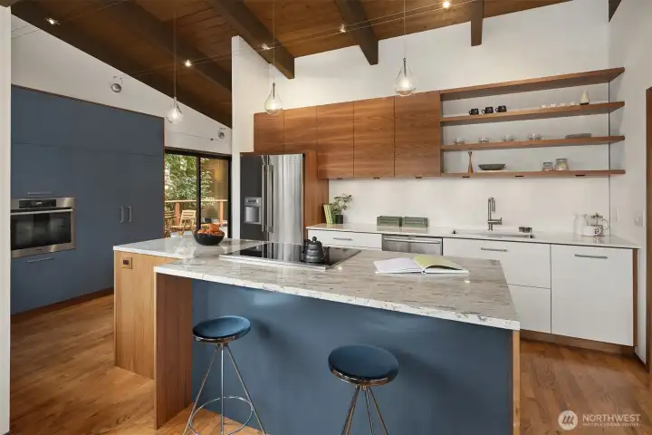 Note the carefully aligned grain in the beautiful walnut upper cabinets, a mark of truly custom craftsmanship.  Matching walnut shelving offers up display opportunities for your beautiful things.  The blue wall tucked underneath the kitchen island ties it all together with the far pantry/oven wall.