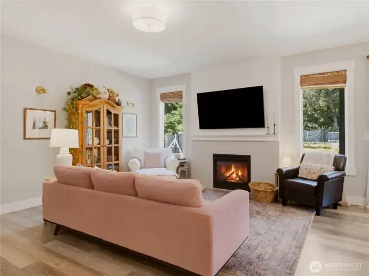 Cozy open concept living space, complete with propane fireplace. Homeowners replaced smaller original picture windows with upgraded full-length windows to allow in light and enjoy peaceful backyard views.