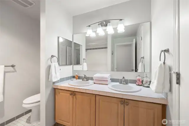 Double vanity, tiled floors, counters and tub/shower surround.