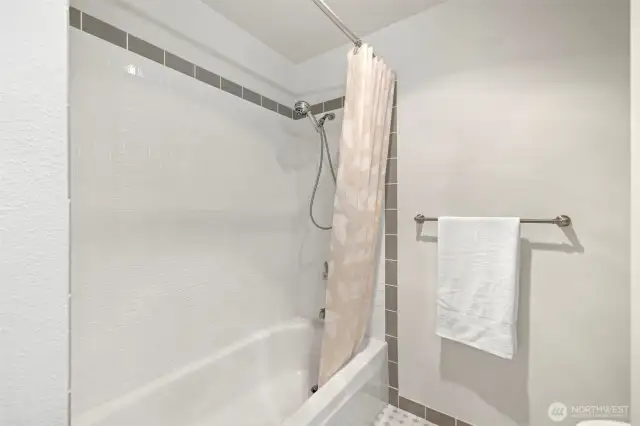 Tiled full shower/tub in spacious bathroom.