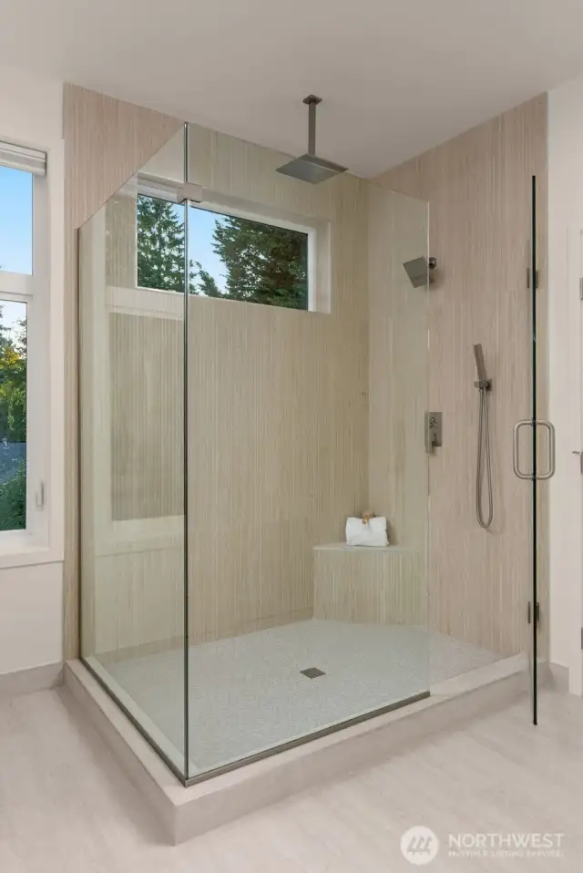 Primary suite walk-in glass surround shower with dual rain shower heads.