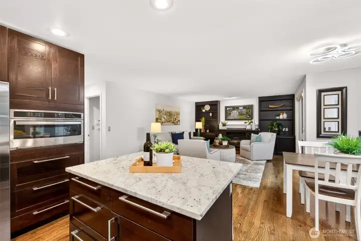 Recessed lighting, warm hardwoods, and an open flow create a kitchen that lives beautifully for both daily routines and entertaining. The island anchors the space while keeping sightlines open to the adjacent gathering areas.