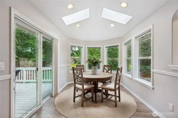 The kitchen adjoins a spacious casual dining area, highlighted by curved panoramic windows that overlook the backyard and skylights above that fill the space with natural light. A sliding glass door opens to the 246sf deck, creating a seamless transition to outdoor living and entertaining.