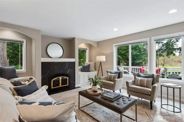 A gas fireplace anchors the room, complete with a large niche above and built in cabinetry alongside. A wall of windows overlooks the back deck and yard, filling the space with natural light and enhancing the connection to the outdoors.