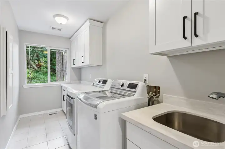 The laundry room features a tile floor and all-new cabinetry, including a spacious folding countertop. A deep utility sink with pull-out faucet, a ironing board cabinet and included washer and gas dryer are added benefits of the home. There is even a laundry chute from the second floor that drops to this room.