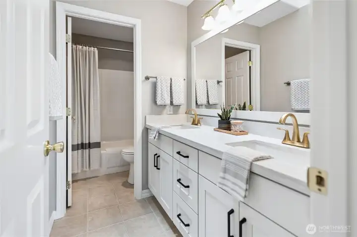 The upstairs bathroom features dual vanities with undermount sinks, quartz countertops and backslash, gold faucets and bath hardware. The tile flooring adds durability and style, while a separate tub and toilet room enhances functionality and privacy.