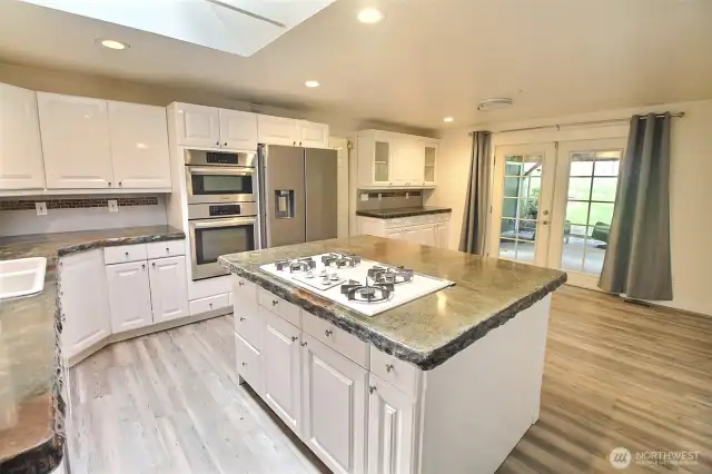 White cabinet kitchen, laminate floor, concrete counter, gas cooking and stainless steel appliances round out this mindful kitchen setup.