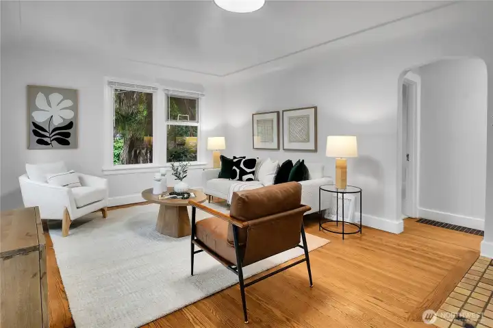 Warm and inviting living room featuring beautiful hardwood floors, expansive windows that fill the space with natural light, and a classic tiled wood-burning fireplace. Warm and inviting living room featuring beautiful hardwood floors, expansive windows that fill the space with natural light, and a classic tiled wood-burning fireplace.