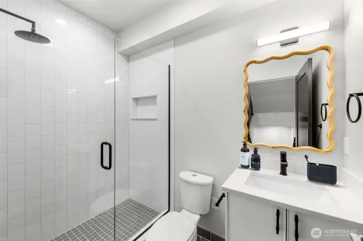 Primary bath, features glass door entry & full tile surround. Continues luxury finishes, quartz countertops, & rainfall showerhead. This image is virtually staged.
