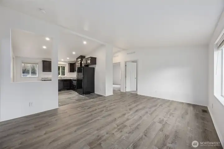 Looking across the living room, the oversized cutout into the kitchen does exactly what good design should, it lets light travel, keeps conversation flowing, and makes the space feel bigger without removing walls entirely. The vaulted ceiling amplifies the effect, while the hallway to the bedrooms stays tucked away. With sunlight pouring in from the front window, this room feels bright, balanced, and easy to live in.
