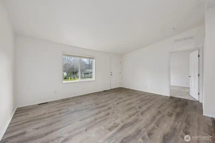 This living room gets its light right. A large front window fills the space with natural daylight, and the included blinds give you instant control over privacy and brightness. Forced air heating keeps the home comfortable and efficient through the colder months, and the open door leads directly into the primary suite for an easy, functional layout. Bright, comfortable, and thoughtfully connected.